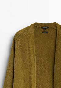 Olivgrön stickad cardigan med öppen front och långa ärmar, visas mot en vit bakgrund.