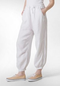 Hvide linned joggerbukser med snoretræk i taljen, sidelommer og elastiske manchetter; parret med lysebeige sneakers.