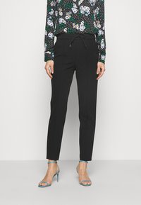 Pantalons noirs ajustés avec une taille élastique, présentant une coupe slim et une texture lisse. Associés à un chemisier à motif floral.