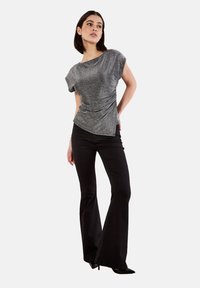 Glänzendes graues Kurzarmoberteil mit drapiertem Design, kombiniert mit schwarzen, ausgestellten Hosen. Glatte Textur und asymmetrisches Saumdetail.
