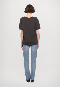 Donkergrijze T-shirthalf met korte mouwen en een ronde halslijn, gecombineerd met lichtblauwe rechte jeans en zwarte enkellaarsjes.