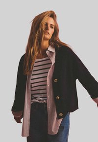 Czarny kardigan z złotymi guzikami nałożony na różową i białą pasiastą koszulę. Niekończące się jeansy dopełniają stylizację. Miękkie materiały, casualowy styl.