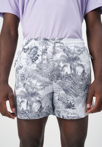 Short swim shorts in light grey fabric with black nature-themed print, featuring an elastic waistband and two side pockets.