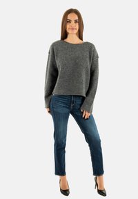 Maglione grigio a maglia con scollo ampio e maniche lunghe, abbinato a jeans blu e scarpe col tacco nere. Texture morbida e vestibilità rilassata.