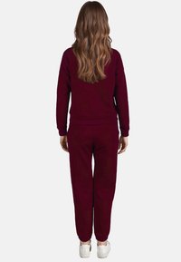 Completo in magenta composto da felpa e pantaloni in tessuto morbido, con polsini e vita a coste, indossato con sneakers bianche, visto da dietro.