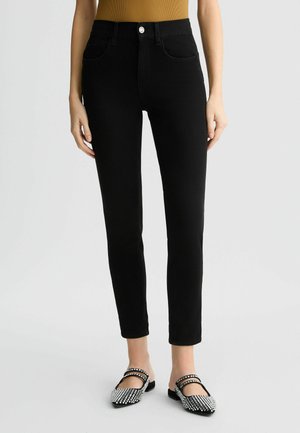 Črne hlače z visokim pasom, gladke teksture in slim fit kroja. Imajo sprednje žepke in srebrno gumbno detajl. Ujemajo se s črnimi in srebrnimi balerinkami.