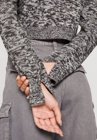 Stickad tröja i svart och vitt melerat mönster, med en kort design och delade ärmar. Matchas med grå texturerade byxor.