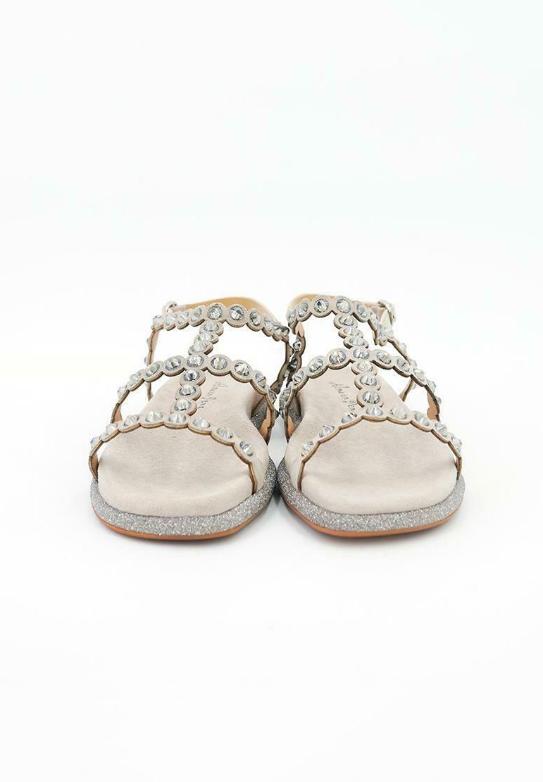 Sandalias beige con acabado de ante, que presentan tachuelas plateadas decorativas y una suela brillante. Diseño de punta abierta y correas entrelazadas.