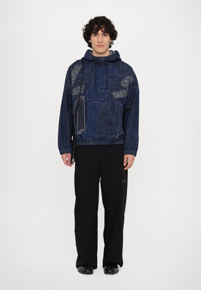 Haut à capuche bleu marine avec motif graphique dans des teintes plus claires, doté d'une capuche avec cordon de serrage et de poignets côtelés, associé à un pantalon large noir.