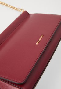 Sac en cuir bordeaux à bandoulière avec une chaîne en or et un petit logo Michael Kors en or sur le rabat avant.
