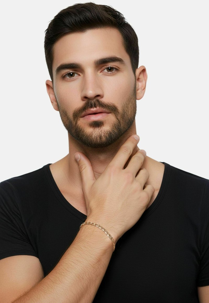 Gouden armband om een hand met een zwart shirt met korte mouwen. De armband heeft ronde schakels die in een eenvoudig patroon zijn gerangschikt.