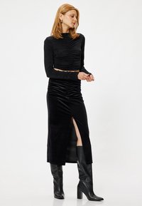 Zwarte lange mouwen top met geplooide details en glitters, gecombineerd met een zwarte fluwelen midi rok met een zijsplits, gedragen met zwarte laarzen tot de knie.