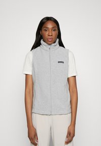 Harmaa fleece-liivi, jossa on korkea kaulus, vetoketjukiinnitys ja logopatch. Käytetään vaalean värisen T-paidan päällä, jolla on pehmeä rakenne.