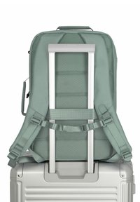 Un sac à dos vert menthe avec des sections rembourrées, des bretelles réglables et une poignée supérieure, monté sur une valise à roulettes argentée avec une poignée rétractable.