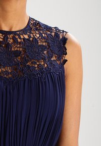 Navy blue dress featuring a pleated skirt and a floral lace bodice with intricate embroidery detailing and a rounded neckline.