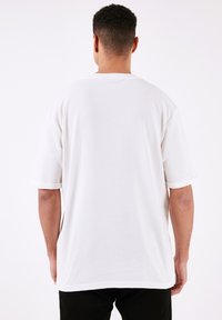Tricou alb cu maneci scurte, cu croi lejer, textură canelată și mansete în contrast. Spate simplu cu un detaliu de crăpătură pe lateral la margine.