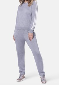 Sudadera gris y pantalones jogger de tela suave, con franjas laterales blancas. El conjunto incluye zapatillas deportivas con suela acolchada.