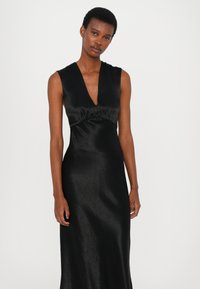 Rochie din satin negru cu un decolteu adânc în V, design fără mâneci și corset ajustat. Țesătura are o textură subtilă și o siluetă fluidă.