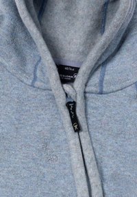 Hoodie i ljusblå fleece med dragkedja och texturerad tyg. Broderad logotyp på framsidan nära dragkedjan.