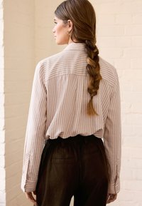 Chemise à rayures roses claires à boutons, manches longues, coupe décontractée, avec un empiècement au dos, associée à un pantalon sombre à taille élastique.