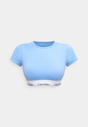 Hellblaues kurzes T-Shirt aus weichem Stoff mit kurzen Ärmeln. Am unteren Rand befindet sich ein weißes Band mit dem "Calvin Klein"-Logo.