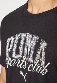 Camiseta de algodón negra con impresión desgastada en blanco que dice "club deportivo PUMA" y su logo. Cuello redondo y mangas cortas.