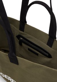 Borsa tote in canvas verde oliva con manici neri, dotata di una tasca con zip e texture liscia, che presenta un design minimalista.