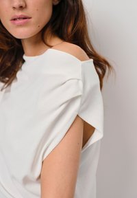 Witte katoenen t-shirt met een off-shoulder ontwerp en omgerolde korte mouwen, met een zachte textuur en minimale stikdetails.