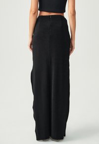 Melnā maksi svārki ar pieguļošu jostasvietu, izgatavoti no gludas auduma. Satur aizmugurējo rāvējslēdzēju un sānu šķeltnes, lai nodrošinātu papildu kustību.