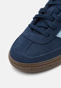 Navy suede sneaker featuring a textured upper, contrasting light blue accents, flat laces, and a gum rubber outsole with diamond pattern.