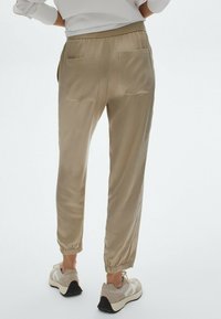 Beige joggerbukser med elastisk talje, tapered ben og to baglommer. Glat tekstur, parret med lyse sneakers.