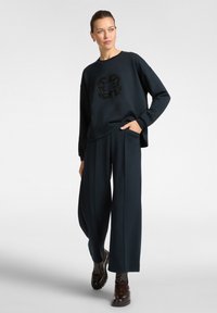 Námořnická mikina s černým korálkovým květinovým motivem; spárována s širokými námořnickými kalhotami; model má na sobě tmavě hnědé masivní boty.