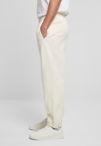Pantaloni de sudură bej deschis cu un waistband elastic, buzunare laterale și o croială relaxată. Terminați cu un detaliu de cusătură subtil la tiv.
