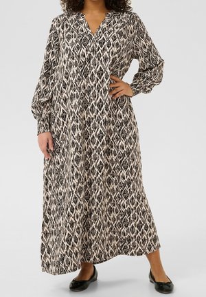 Woman wearing a long-sleeve, black-and-white patterned maxi dress with a V-neck and black ballet flats, standing with one hand on hip.