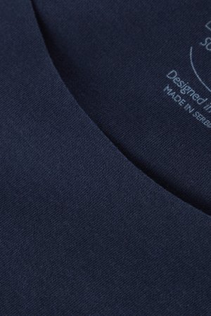 Detailní záběr na tmavě modrou látku s jemnou texturou a hladkým výstřihem; obsahuje potištěný štítek s detaily designu a výroby.