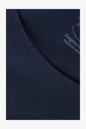 Närbild på marinblått tyg med mjuk textur och en slät halsringning; inkluderar tryckt etikett med design- och tillverkningsdetaljer.