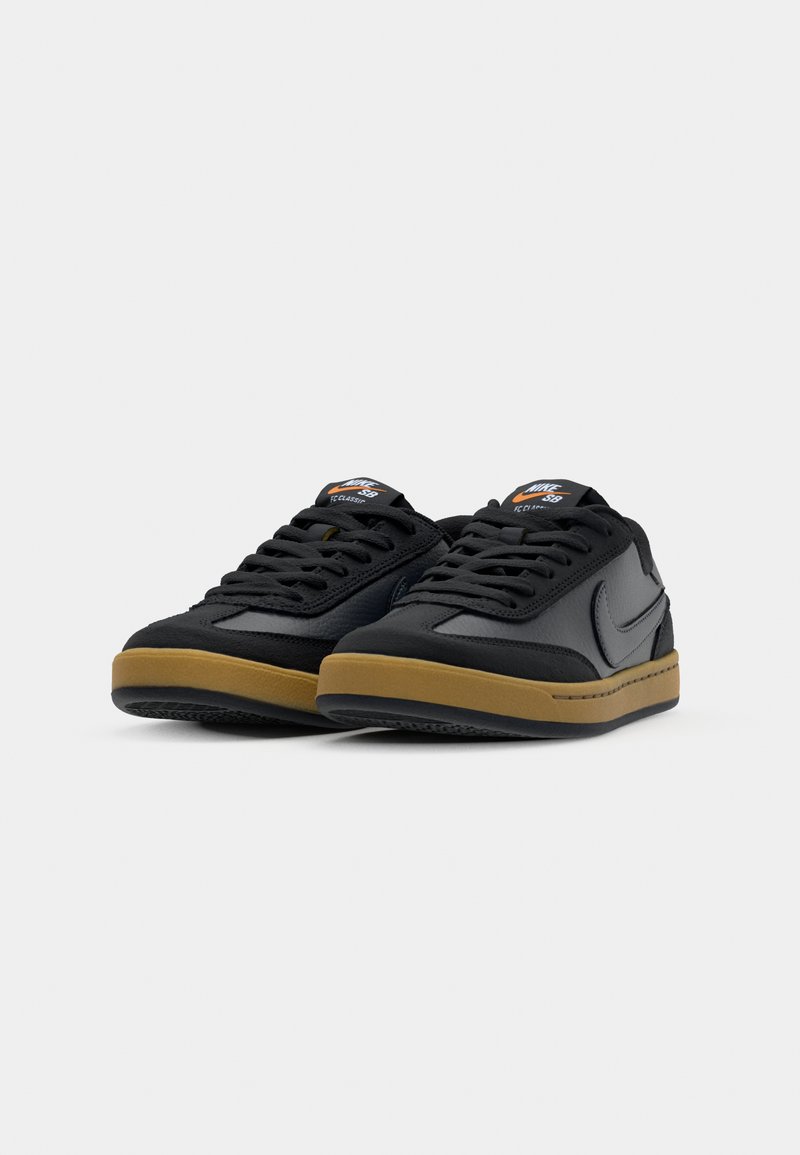 Baskets noires en cuir avec une surface texturée, featuring une semelle en gomme et un logo bien visible sur la languette. Design à lacets.