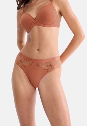 Woman wearing matching burnt orange bra and high-waist panties with lace detailing on a plain background.