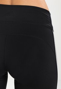 Leggings deportivos negros con cinturilla alta, que presentan sutiles detalles de costura y una franja blanca contrastante a lo largo del lado.