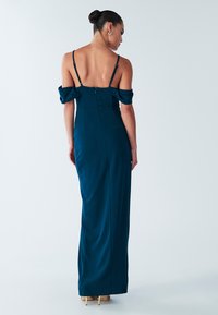 Sininen mekko, jossa olkaimeton malli, vartalonmyötäinen yläosa ja takana piilotettu vetoketju. Sileä kangas ja lattiaan ulottuva pituus.