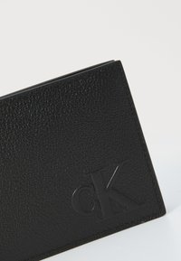 Portafoglio in pelle nera con finitura testurizzata. Presenta il logo "cK" impressocorner, linee pulite e forma compatta.