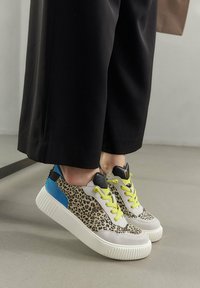 Sneakers w motywem panterki, wykonane z szarego materiału tekstylnego, z niebieskimi akcentami i jasnosłonecznymi sznurówkami. Posiadają grubą, białą gumową podeszwę oraz czarny skórzany obcas.