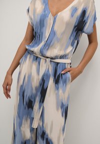 Salopette blu e beige con motivo, scollatura a V, maniche corte e cintura legata in vita. Presenta una texture morbida e fluida e una vestibilità ampia.
