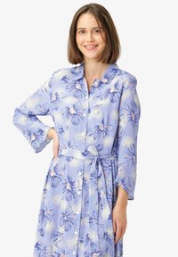 Abito floreale azzurro chiaro con bottoni frontali, maniche lunghe e cintura in vita. Presenta un motivo floreale con accenti di rosa e dettagli metallici.