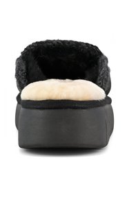 Pantofole nere senza lacci con un esterno spesso e texture nera e una morbida fodera in pile crema, dotate di una suola nera bassa e resistente.