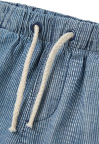 Shorts en denim bleu clair avec des rayures verticales, dotés d'un cordon de serrage avec des extrémités beiges et des œillets bleu marine. Comprend un détail de poche latérale.