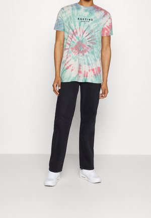 Koszulka tie-dye w miętowym zielonym, różowym i białym kolorze z spiralnym wzorem oraz czarnym napisem "KAOTIKO Since 1999". Czarne spodnie i białe sneakersy.