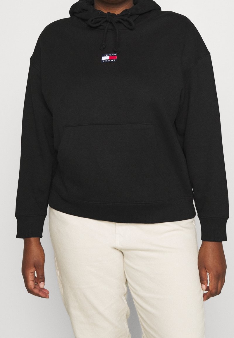 Sudadera negra de tela suave, con un bolsillo canguro en la parte frontal y una capucha ajustable con cordones. Pequeño logo de la marca en el pecho.