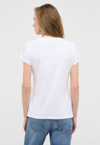 White short-sleeve t-shirt made of cotton, featuring a round neckline and subtle stitching detail around the hem. Worn with blue denim jeans.