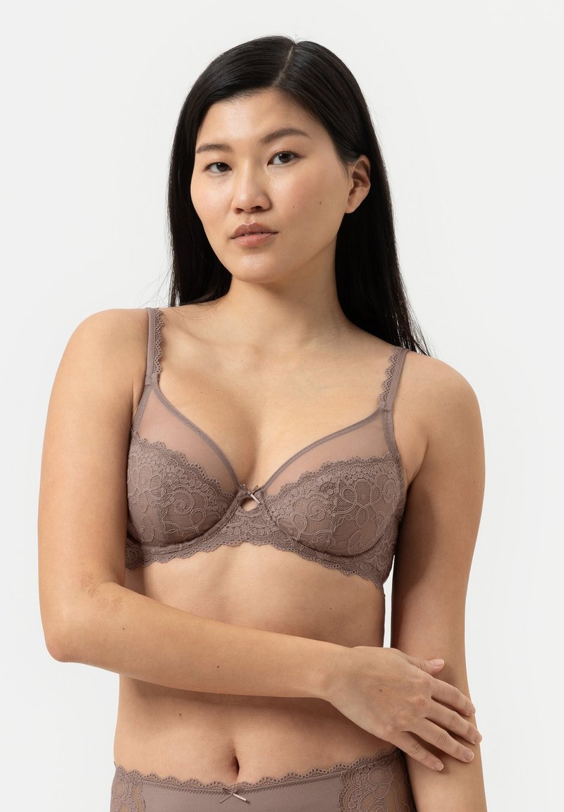 Brun bh med spetsdetaljer, genomskinliga kupor, en delikat mittslips och justerbara band. Mjuk textur och blommönster.